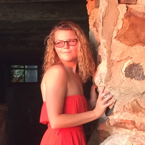 young woman in glasses leaning toward stone wall