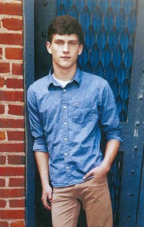 young man leaning up against door with one hand in his pocket