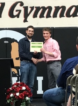 two men holding up a piece of paper and shaking hands on stage