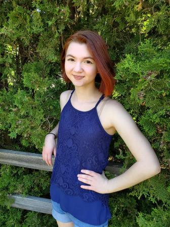 young woman leaning on wooden fence in front of bushes