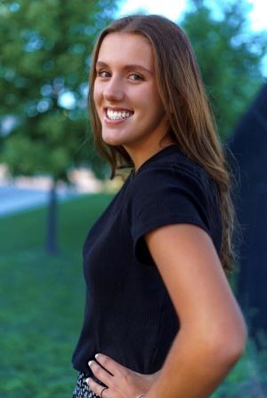 smiling young woman with hands on hips in front of trees
