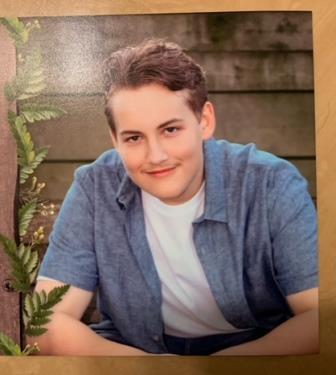 smiling young man posing in front of wood sided building